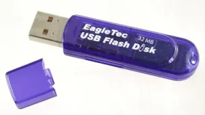 A purplish blue semi-transparent plastic electronic device with a USB plug sticking out of it. White text printed on it reads: EagleTec USB Flash Disk 32 MB.