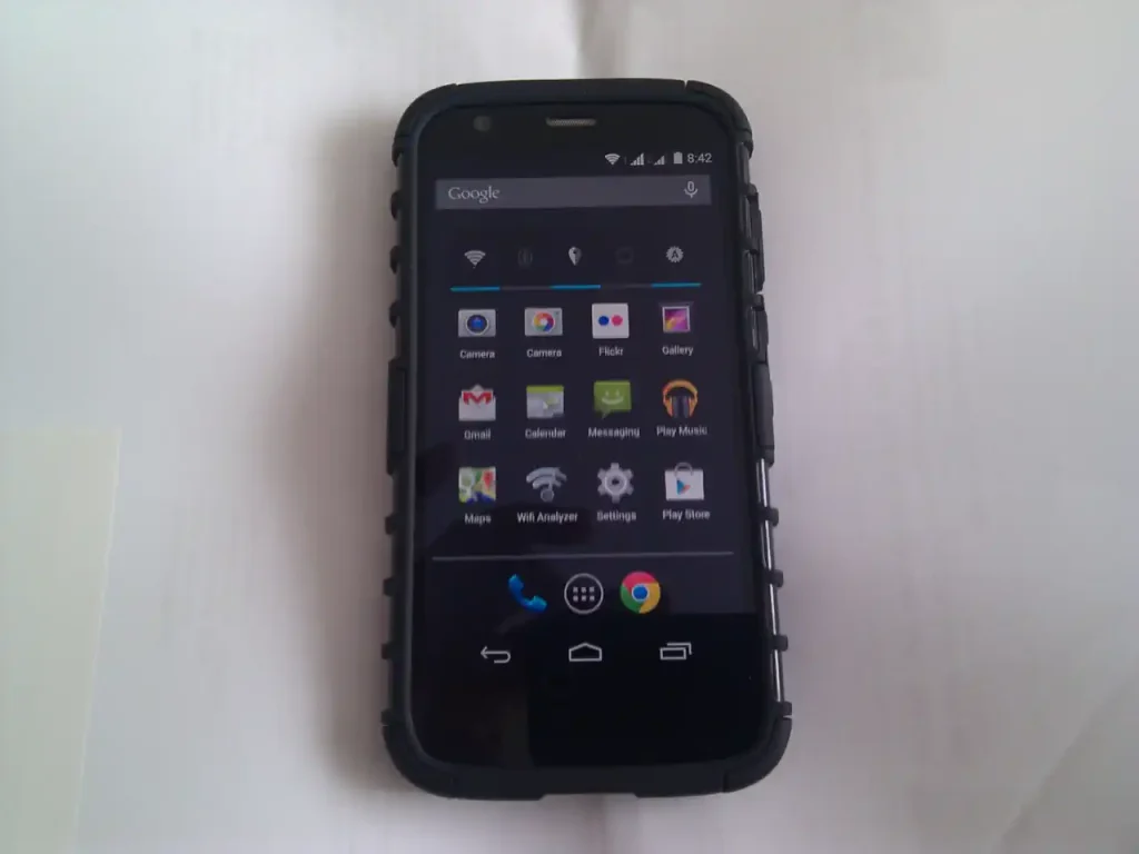 A photo of a smartphone displaying icons of various applications and a Google search bar. The applications are: Camera, Camera (again), Flickr, Gallery, Gmail, Calendar, Messaging, Play Music, Maps, Wifi Analyzer, Settings, and Play Store.